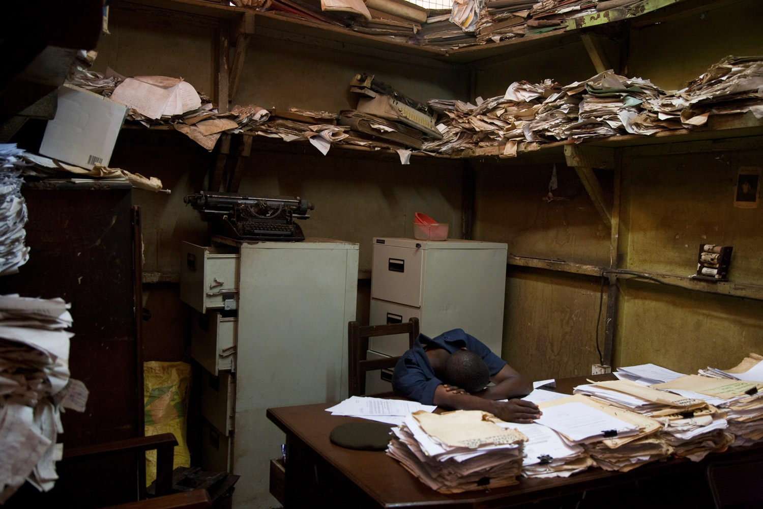 A prison officer rests in the registration room, among the chaos of the prisoner records. Similar names and surnames, as well as carelessness and negligence on the part of the officers, complicates the process for inmates. Many remain in jail for years before their trial even starts.