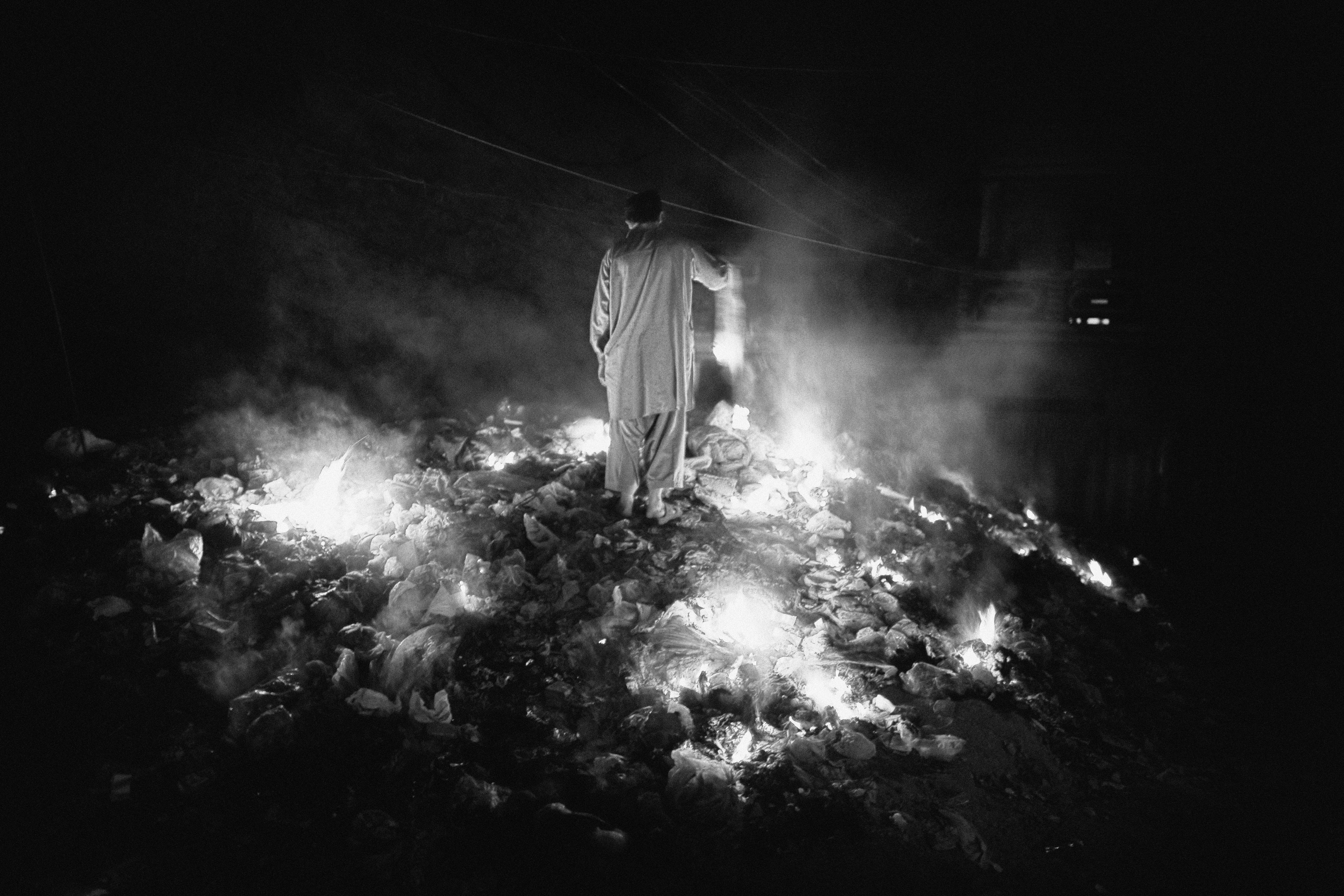 A man standing on a burning pile of garbage in Rawalpindi District, Pakistan.
                              March 2009.