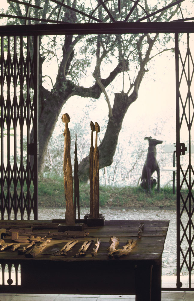 Bronze replicas of Picasso's elongated wood statuettes sit on a table in his Mougins workshop; out the window, a sculpture of a dog (1967).