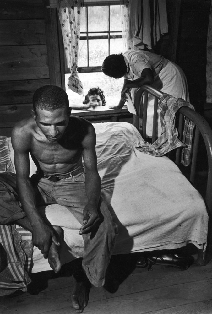 Caption from LIFE. Tuberculosis case, 33-year-old Leon Snipe, sits morosely on bed while Maude arranges with his sister for him to go to state sanatorium.