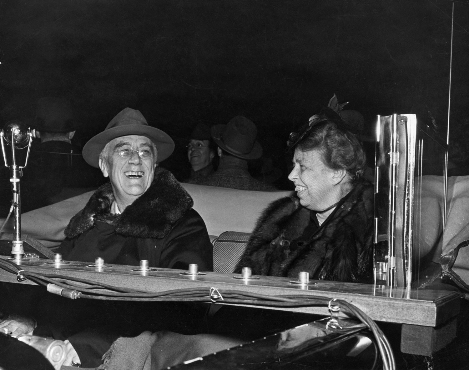 President Franklin D. Roosevelt and his wife Eleanor in front of broadcast microphones mounted on a plank across the backseat of their limousine during a stop in Hyde Park, NY, 1944.