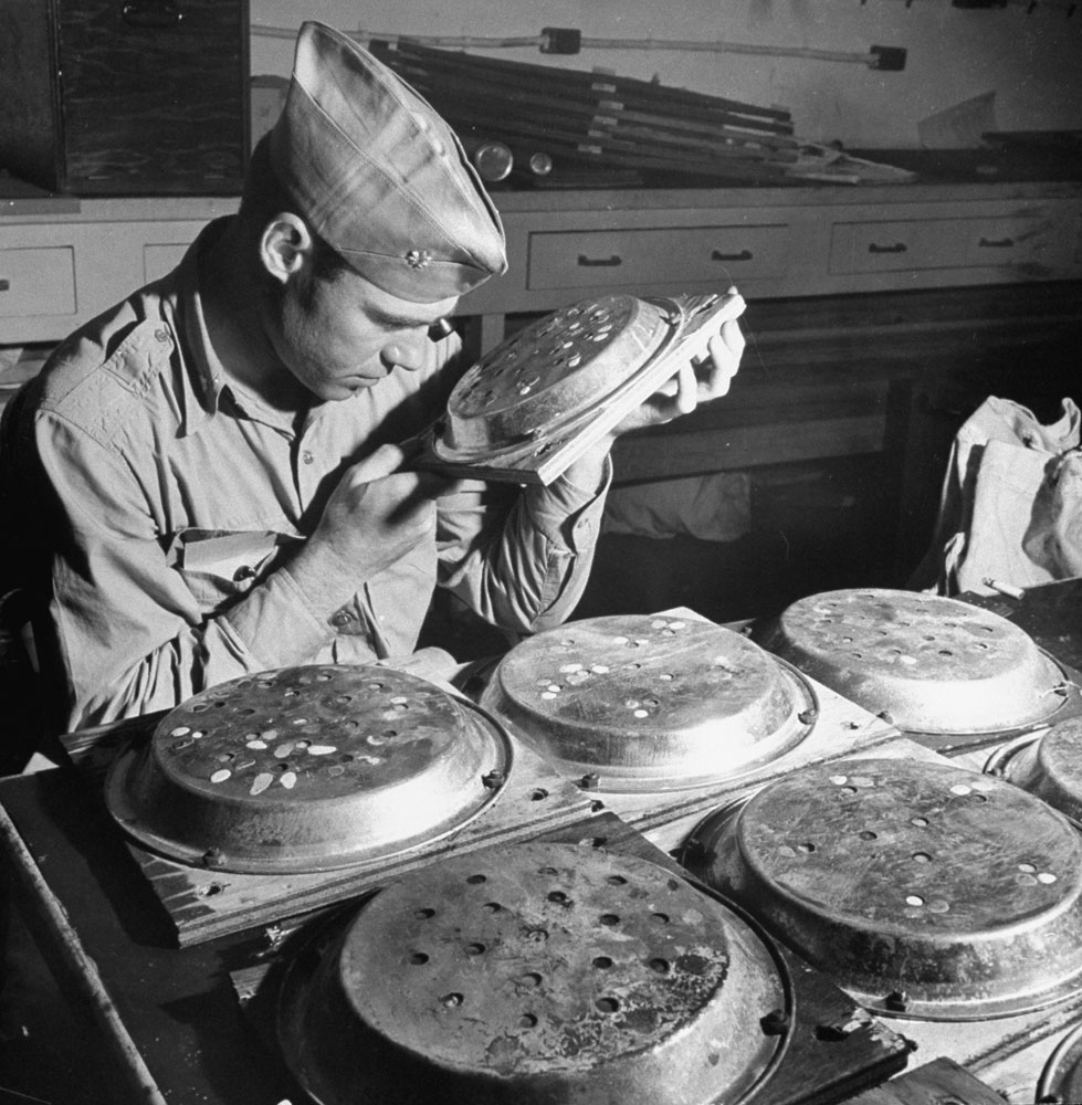 A scientist examines samples of minerals on boards covered with pie pans that were exposed to radiation during a test nuclear explosion in the South Pacific, 1946.