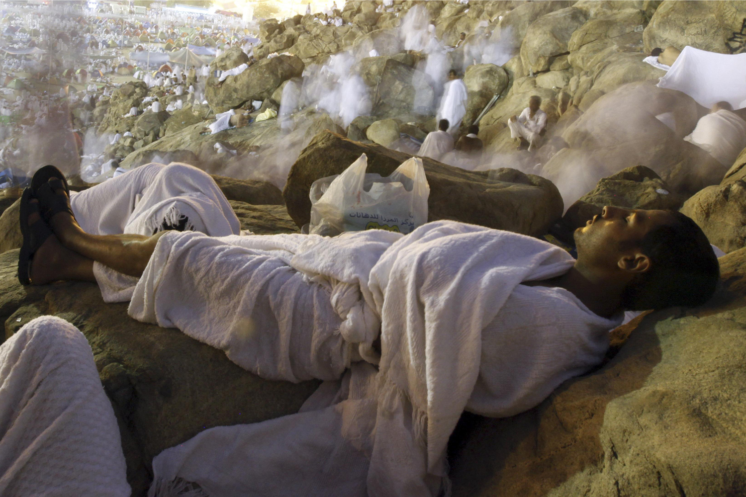 Image: Oct. 25, 2012. A Muslim pilgrim sleeps while others climb Mount Mercy on the plains of Arafat in the early morning during the peak of the annual haj pilgrimage near the holy city of Mecca.