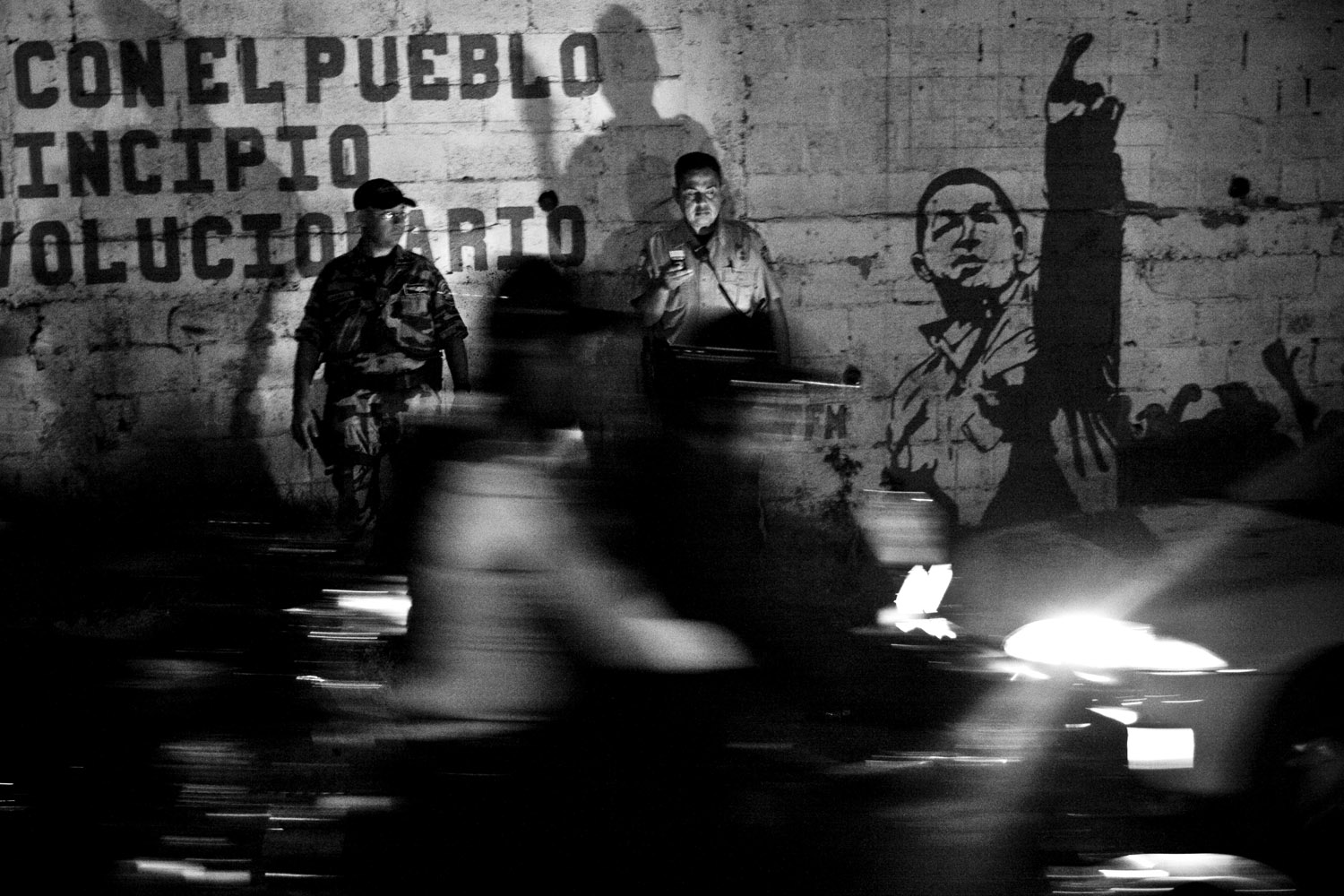 Sucre police officers stand at a checkpoint in front of graffiti of Hugo Chavez.