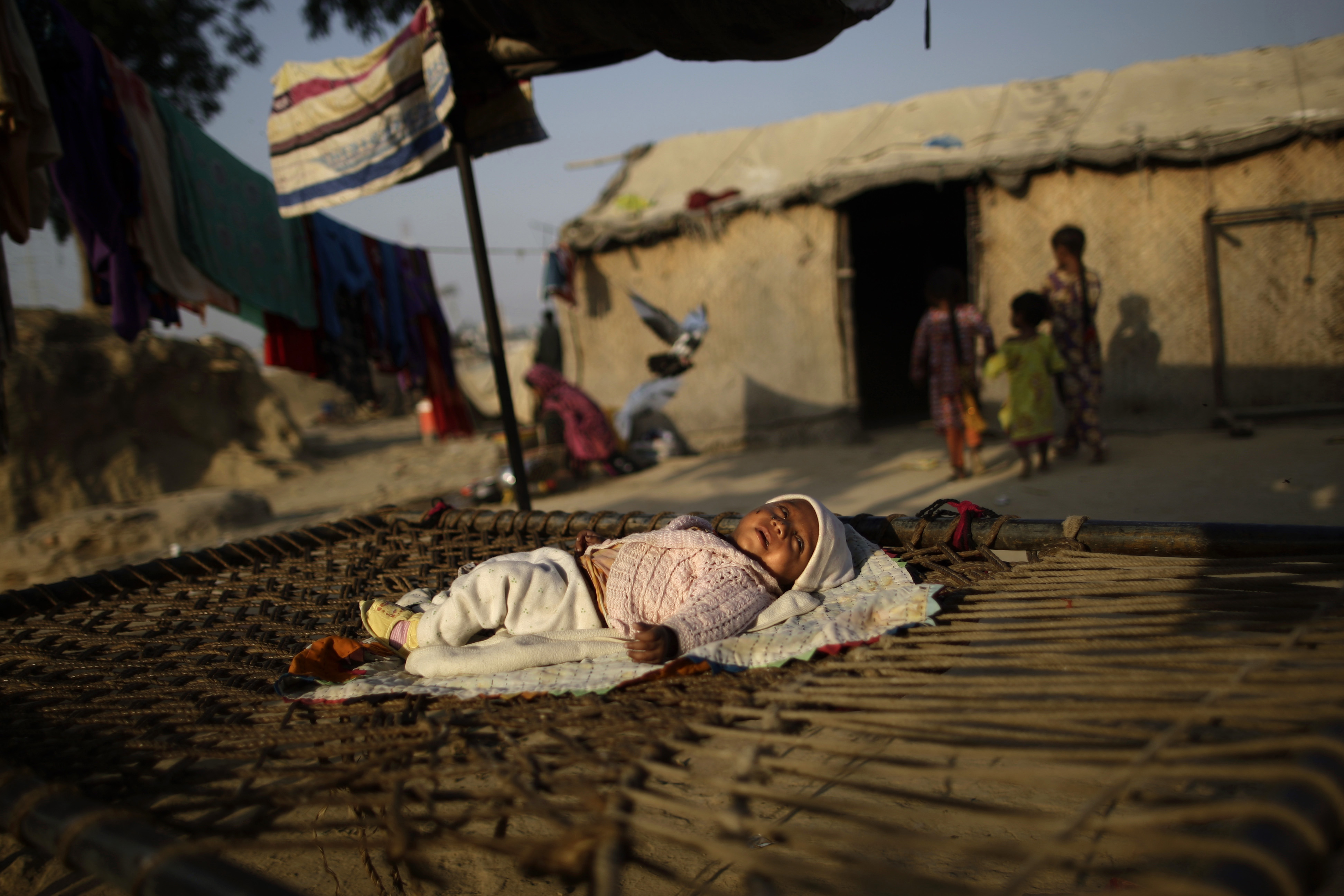 Oct. 8, 2012. A Pakistani child who was displaced from a village in Pakistan's Sindh province by floods in 2010, lies on a bed inside his family's makeshift home, while his mother cleans dishes in a slum on the outskirts of Islamabad.