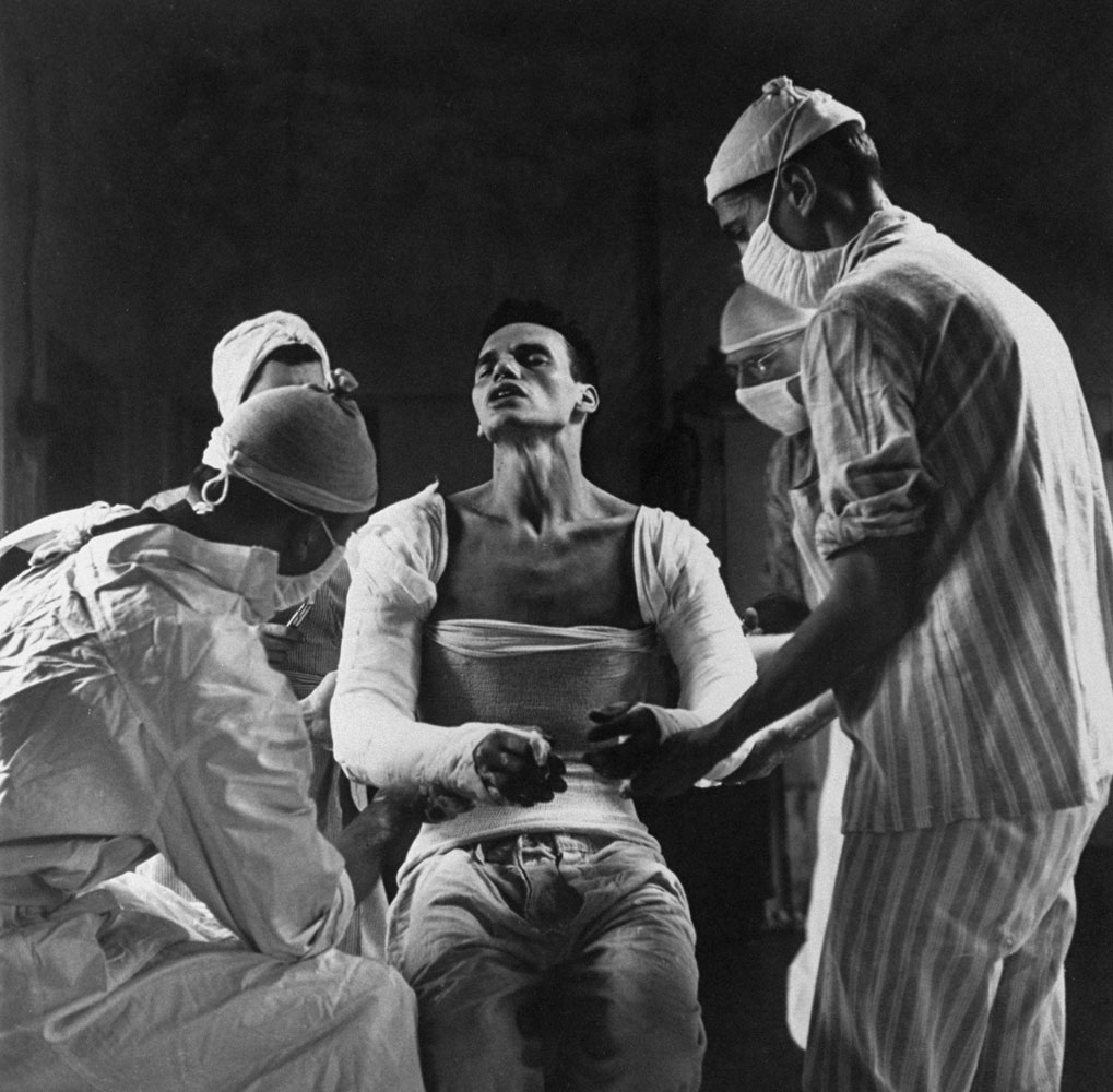 George Lott, 22, wounded in both arms by German mortar fire, suffers as doctors mold a plaster cast to his body, 1944.