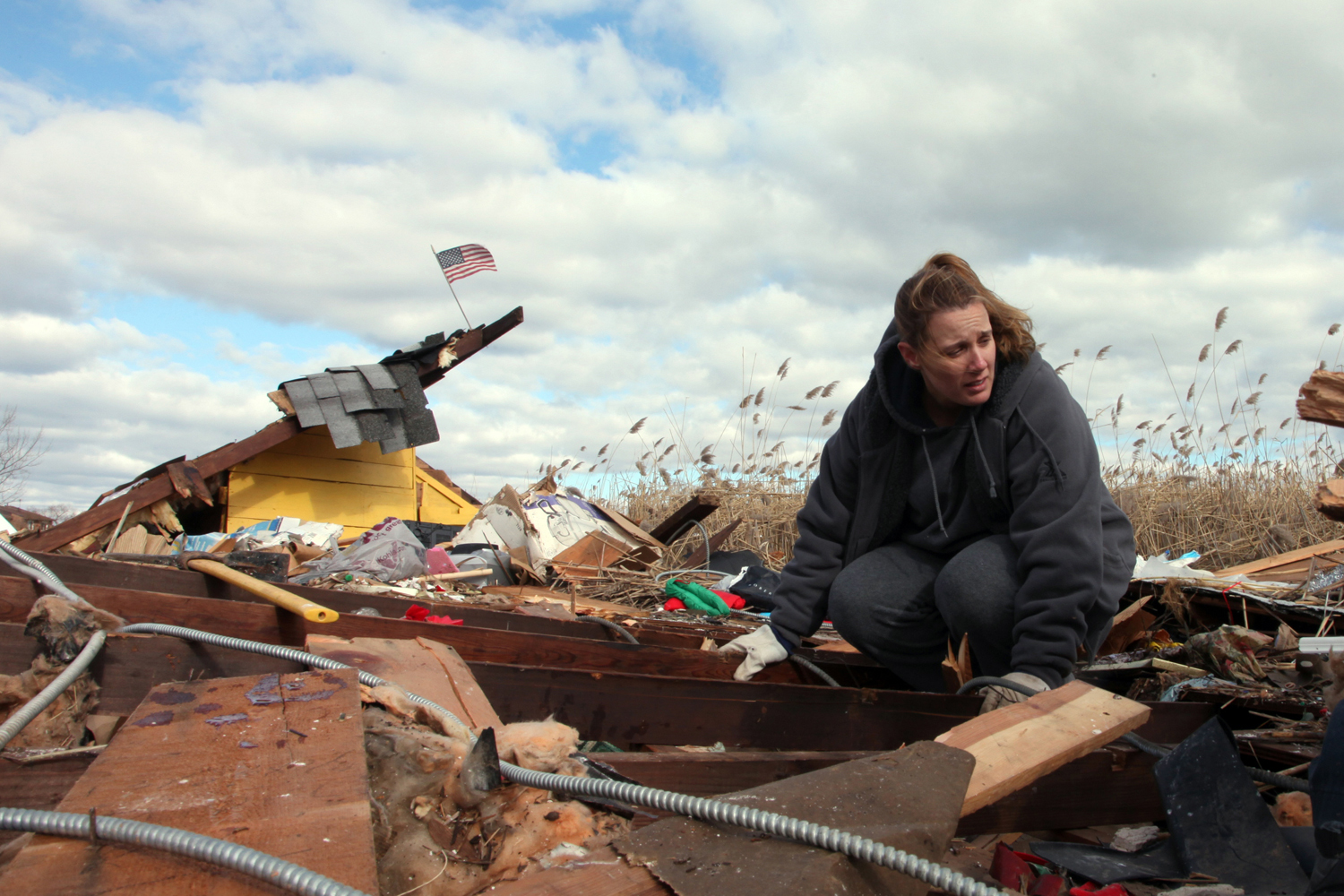 Image: Nov. 3, 2012. Susan Aman searches through the remains of her father’s home, which had been located on Kissam Avenue, but was carried by the flood water into the marsh along Mill Road. She believes that she is crouching on top of what had been her father’s bedroom.