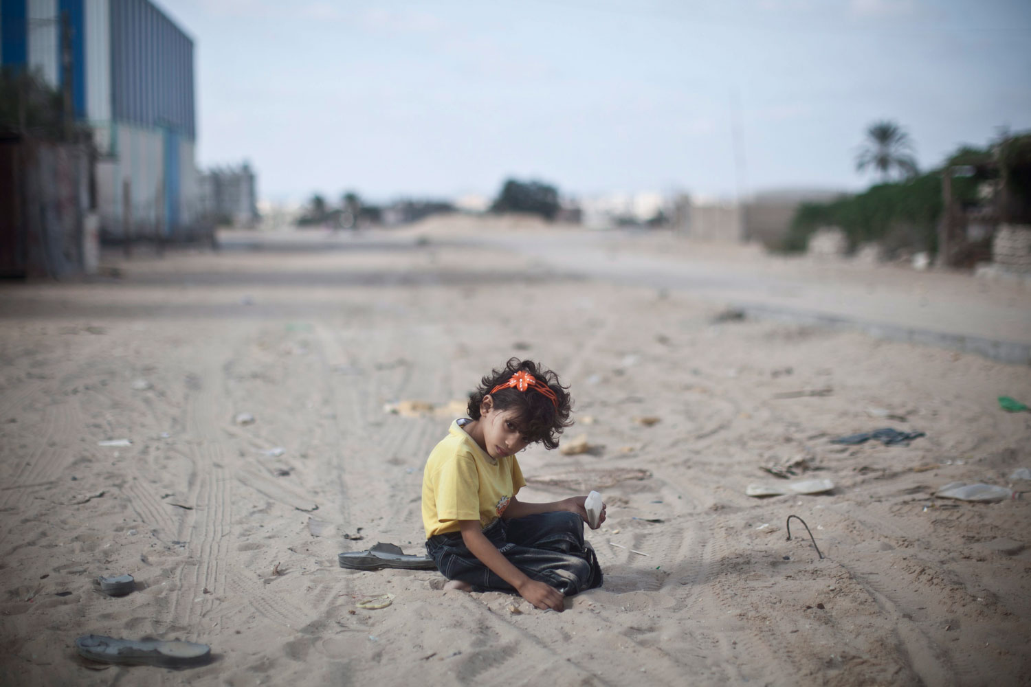 Image: Nov. 7, 2012. A young Palestinian girl plays with sand on a littered road in the Al-Shabora refugee camp in Rafah, southern Gaza.