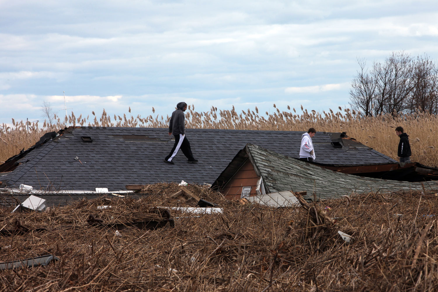 Image: Neighborhood teens walk along roofs of houses that were carried by floodwater into the marsh along Mill Road.