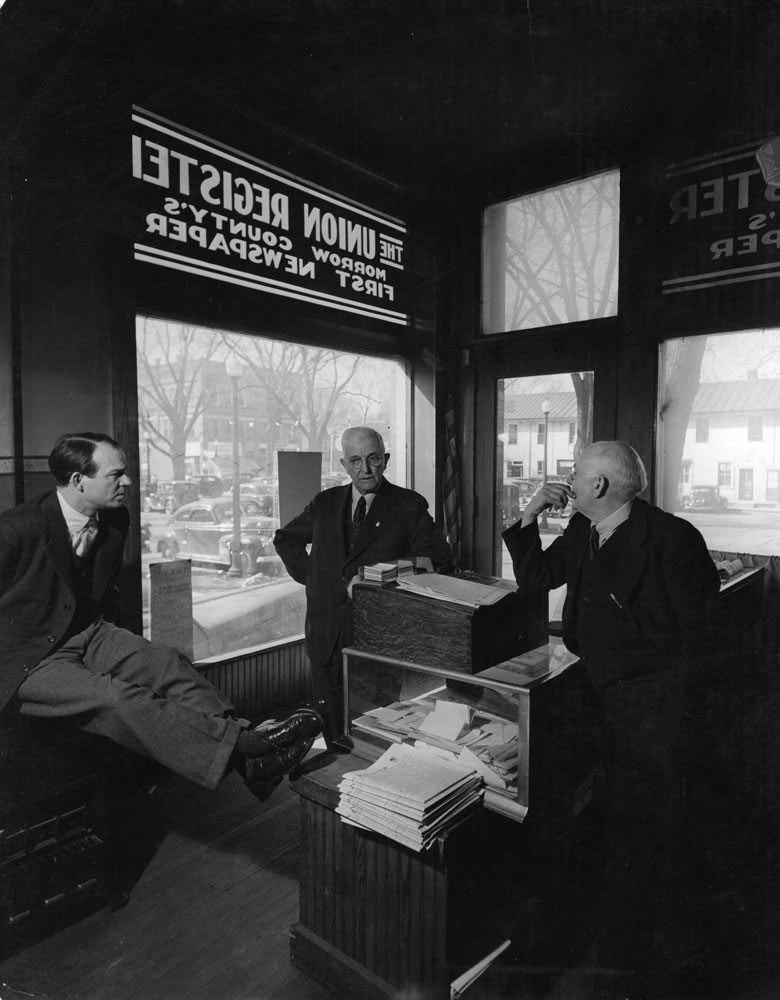 Publisher W. R. Conway of the Monroe County Union Register, which put out three weeklies -- one Democrat, one Republican and one "liberal" -- chats over his counter with Mt. Gilead, Ohio, mayor Ray Booker, 1944. The Union Register was the one Democratic paper in the largely Republican county.