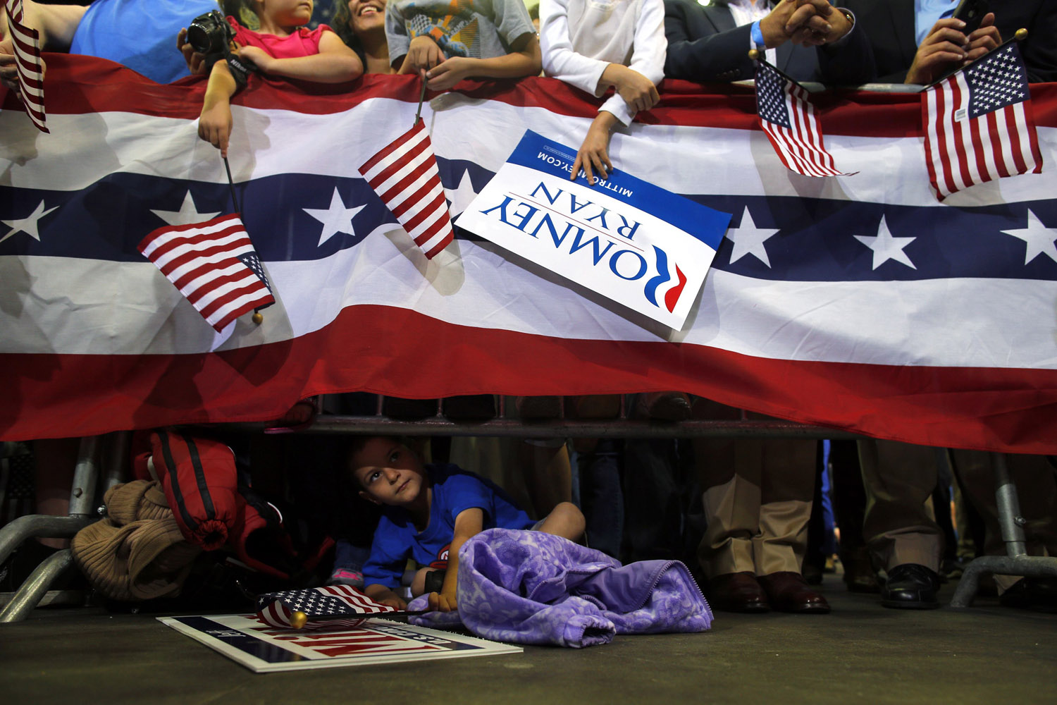 Image: Oct. 27, 2012. A young boy looks out from under the barrier at the edge of the stage as Republican presidential nominee Mitt Romney speaks at a campaign rally in Pensacola, Fla.