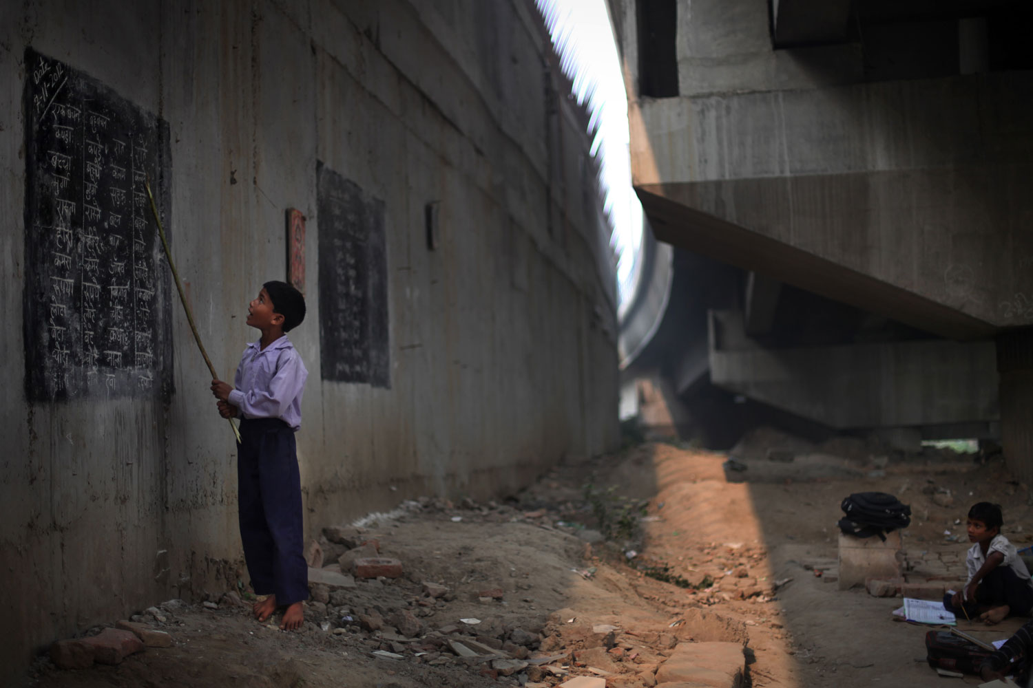 Image: Nov. 7, 2012. Indian child Rajesh, 8, reads from a black board painted on a building wall at a free school run under a metro bridge in New Delhi.