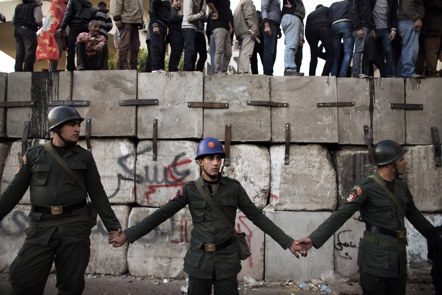 Dec. 11, 2012. Egyptian soldiers form a line in front as protestors against Egyptian President Mohamed Morsi stand atop barricades erected by the army to protect the Presidential Palace in Cairo. Demonstrators gathered for rival rallies over a deeply disputed constitutional referendum proposed by President Morsi.