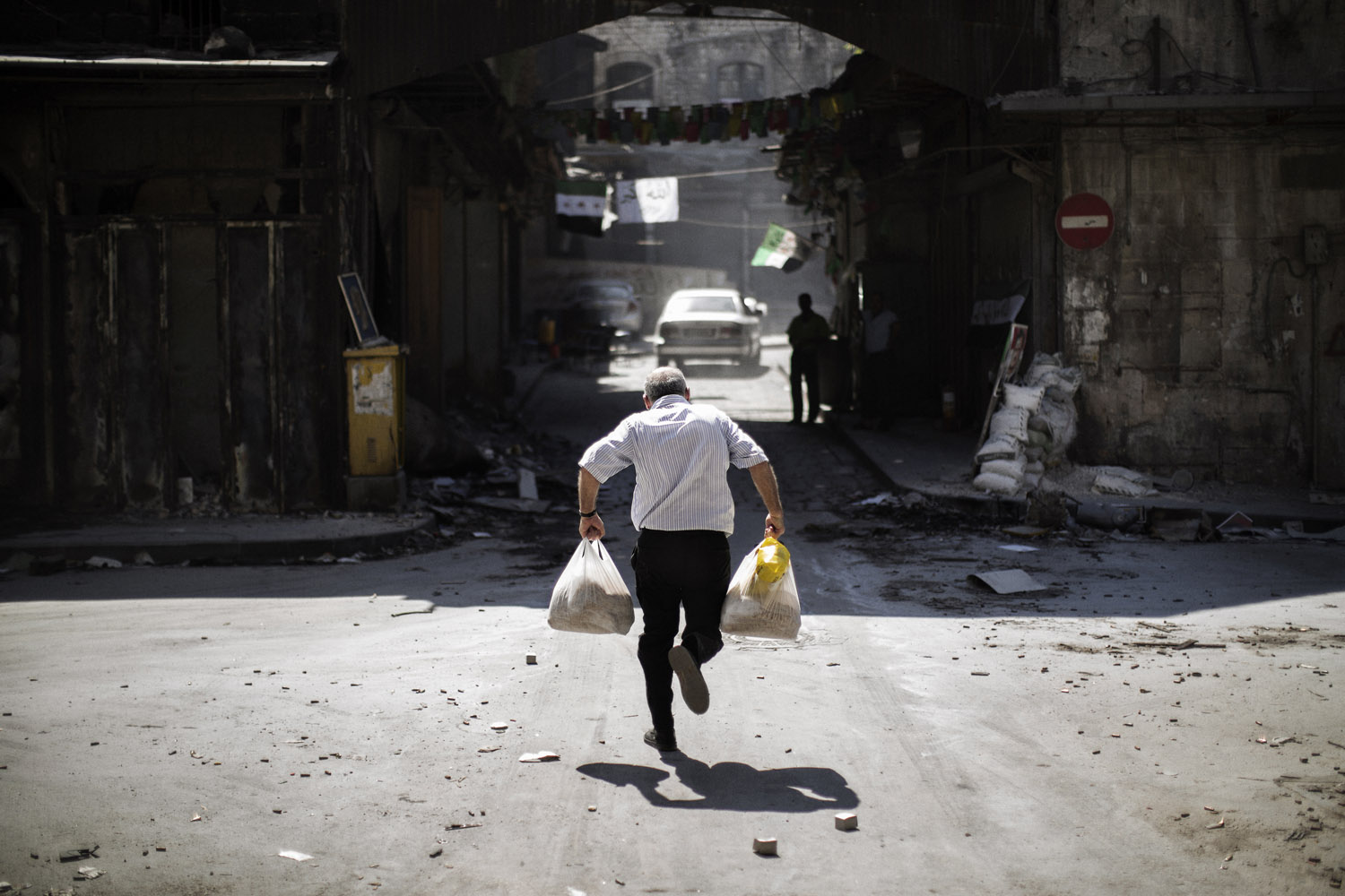 Sept. 14, 2012. A Syrian man carrying grocery bags tries to dodge sniper fire as he runs through an alley near a checkpoint manned by the Free Syria Army in Aleppo, Syria.