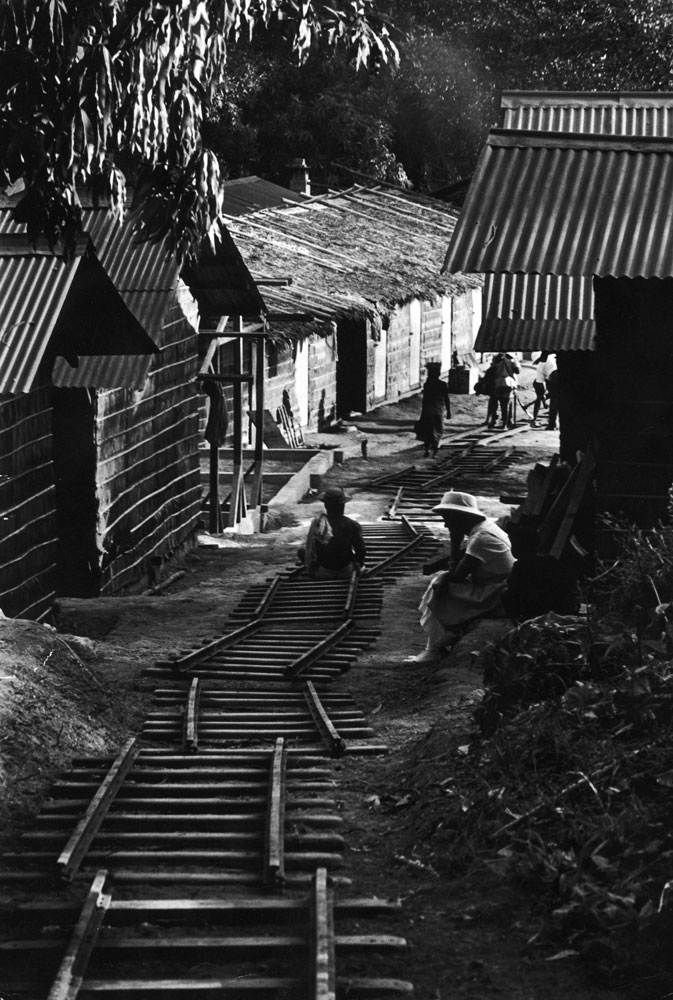Portable railroad, lent by a nearby plantation owner, is set down in the main street of the leper village for a major project in earth moving.