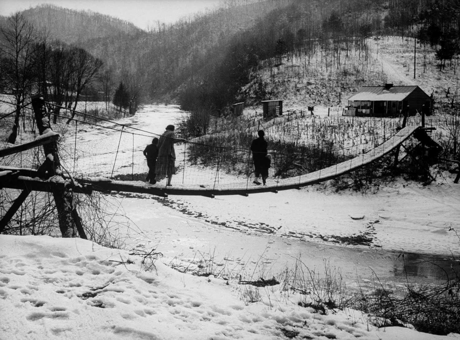 On a wintry afternoon in Line Fork Creek a family trudges across a rickety suspension bridge over a sewage-polluted stream to its two-room shack.