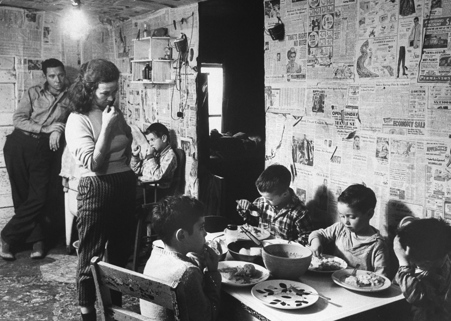 Youngsters lap up a surplus-commodity supper of pan-fried biscuits, gravy and potatoes at the Odell Smiths of Friday Branch Creek. The newspapers were pasted by Mrs. Smith in an effort to keep the place neat.