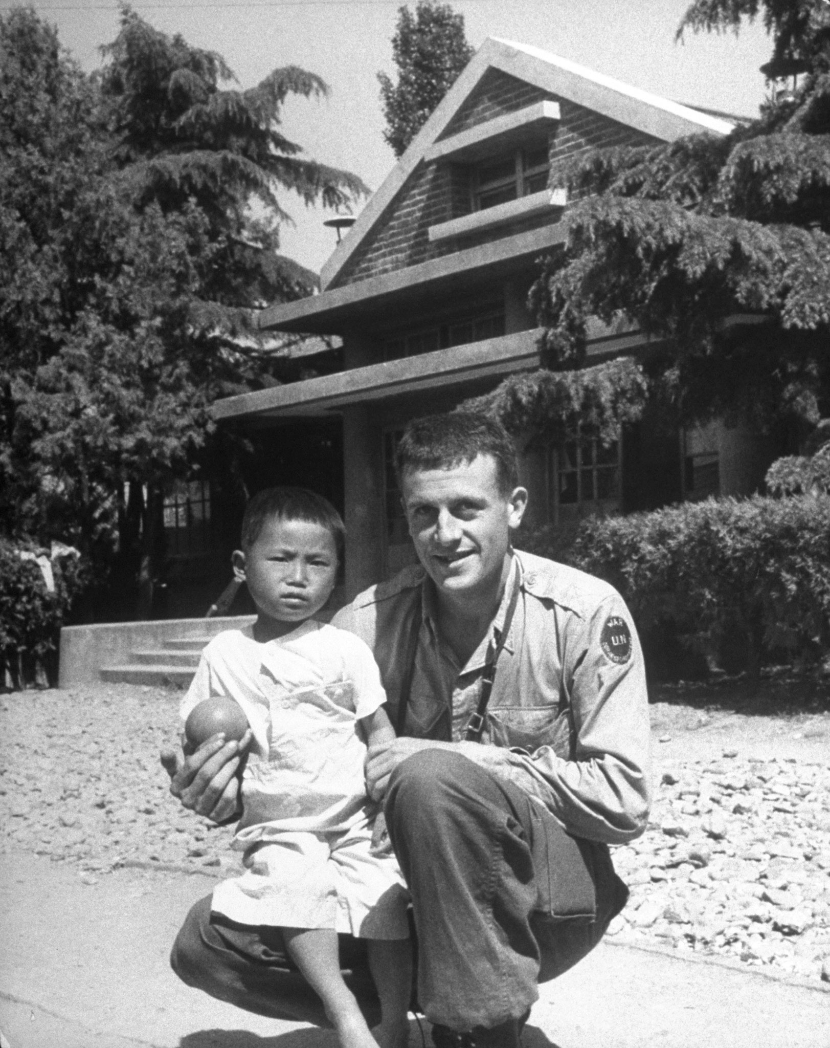 LIFE photographer Michael Rougier, kneeling on ground with a Korean orphan.