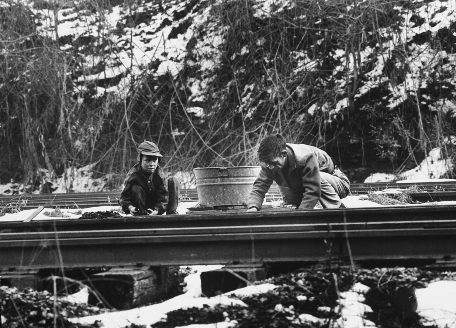 Tearing with bare hands at frozen lumps of coal, Willard Bryant and his son Billy crouch between railroad tracks, scavenging fuel to heat their home. When the tub is full, they will drag it to the hill where they live, reload the coal into bags and carry it on their backs to the house.