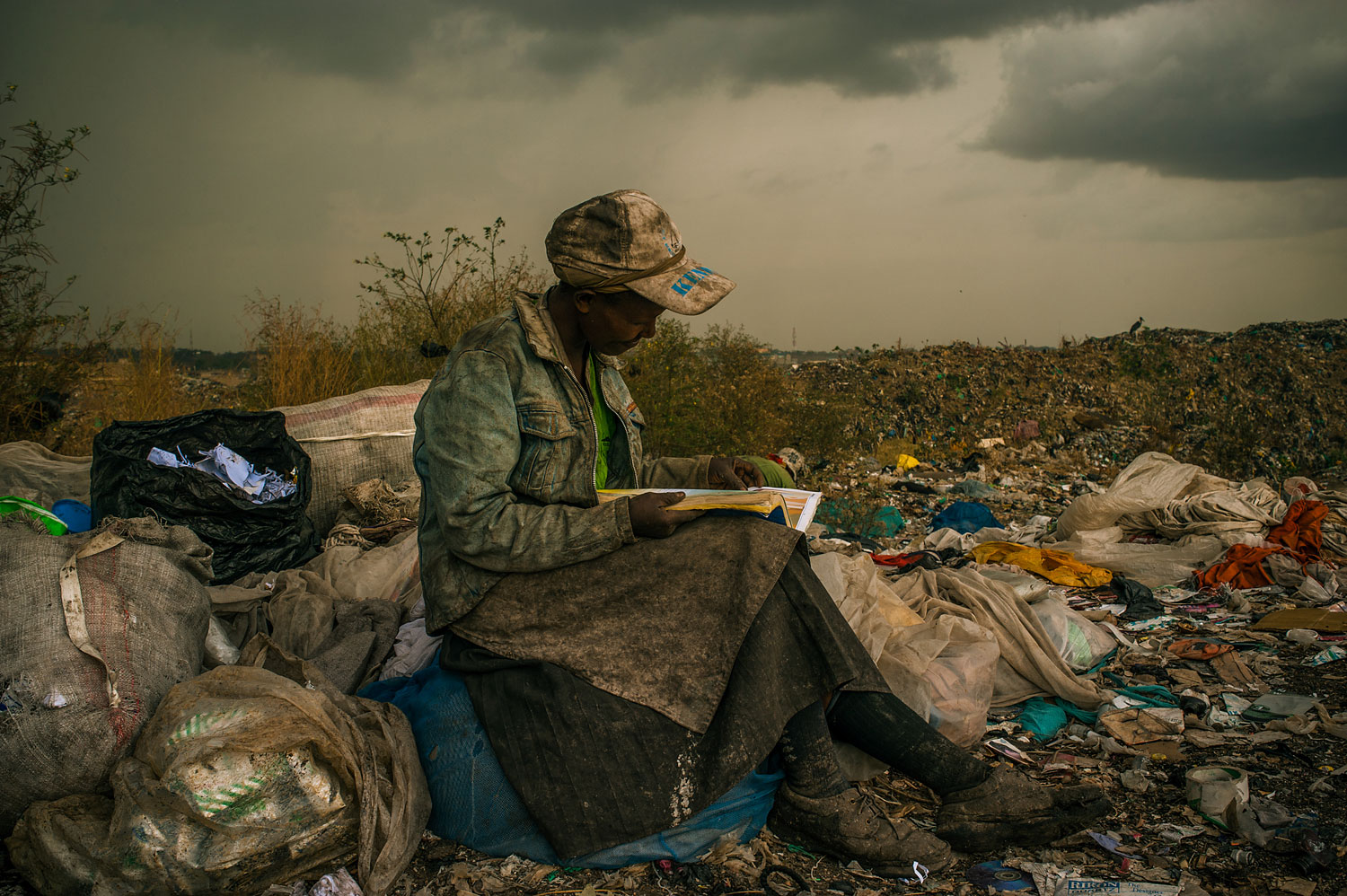 1st Prize Contemporary Issues Single. Micah Albert, USA, Redux Images. 3 April 2012, Nairobi, Kenya. Pausing in the rain, a woman working as a trash picker at the 30-acre dump, which literally spills into households of one million people living in nearby slums, wishes she had more time to look at the books she comes across. She even likes the industrial parts catalogs. “It gives me something else to do in the day besides picking [trash],” she said.