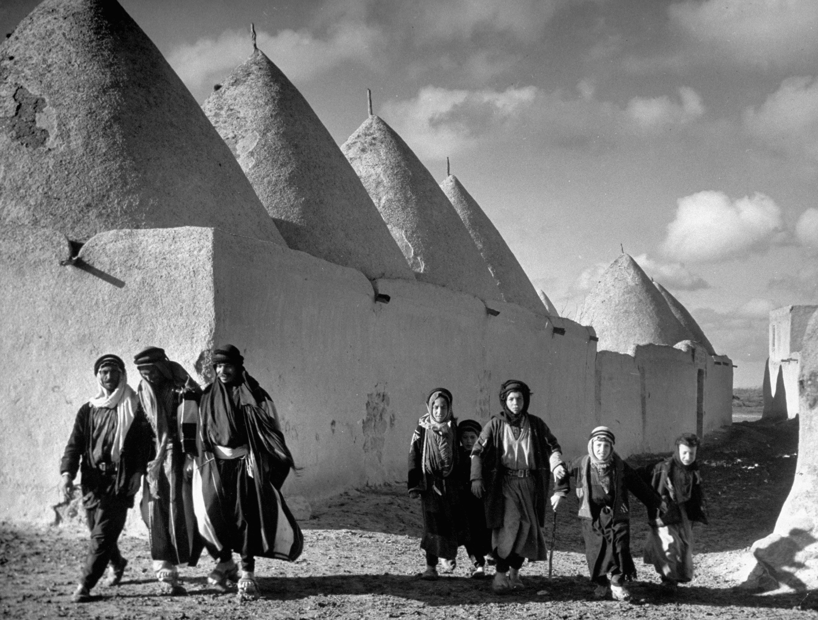 A family walks past the walled town and beehive-shaped homes of Tell Bisse, Syria, 1940.