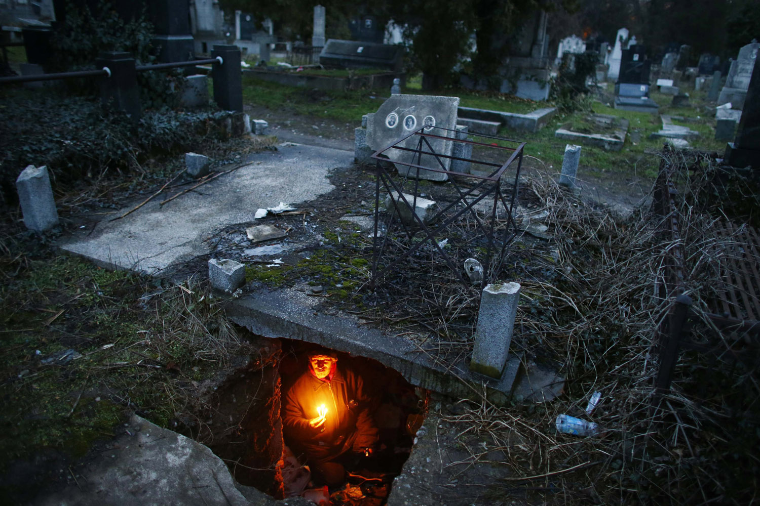 Bratislav Stojanovic, a homeless man, hold candles as sits in a tomb where he lives in southern Serbian town of Nis