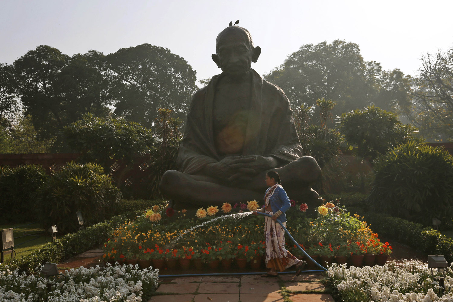 Feb. 28, 2013. A worker waters plants around a statue of Mahatma Gandhi inside the premises of Parliament as Indian Finance Minister Palaniappan Chidambaram delivers the annual budget in New Delhi.