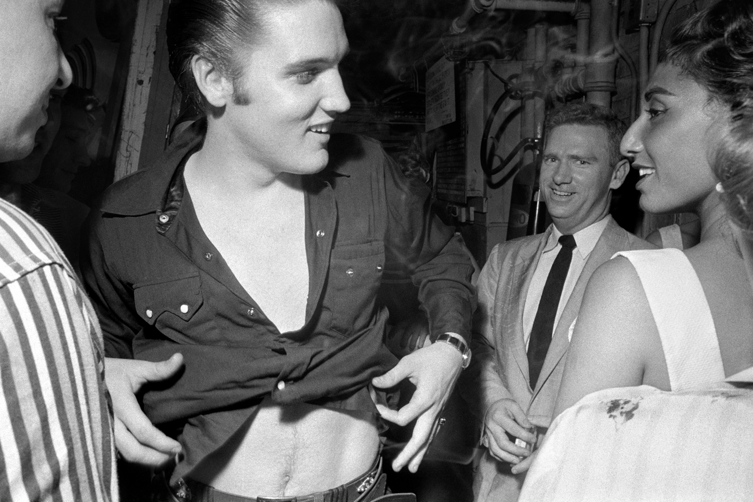 July 1, 1956. The Hudson Theatre, New York. This one was right after the Steve Allen show. Elvis is in his Tumbleweed Presley shirt. He had just played a character in a scripted piece—his first acting roll on TV—and was now getting back into civilian clothes…but then he spots this good looking girl and gets distracted. In the background is Tom Diskin (the Colonel's right hand man) who had originally been offered the deal to be Elvis' manager and turned it down.