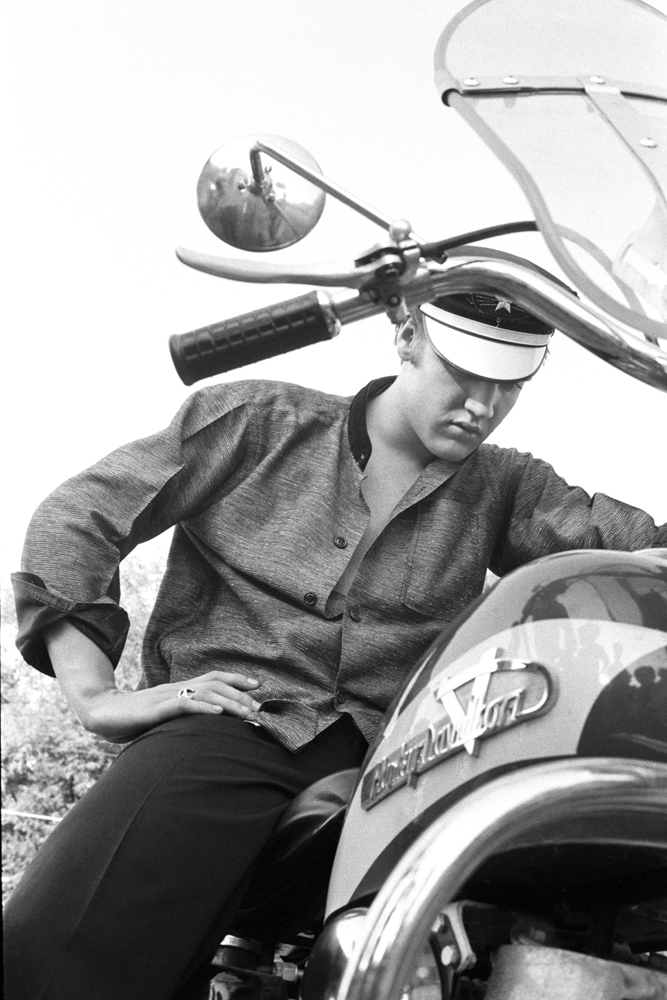 July 4, 1956. 1034 Auburn Drive, Memphis. Elvis  behind his home. This is one of my iconic shots. Everyone says that I posed this, but I swear I didn’t. Why won’t the motorcycle start? No gas in the tank.