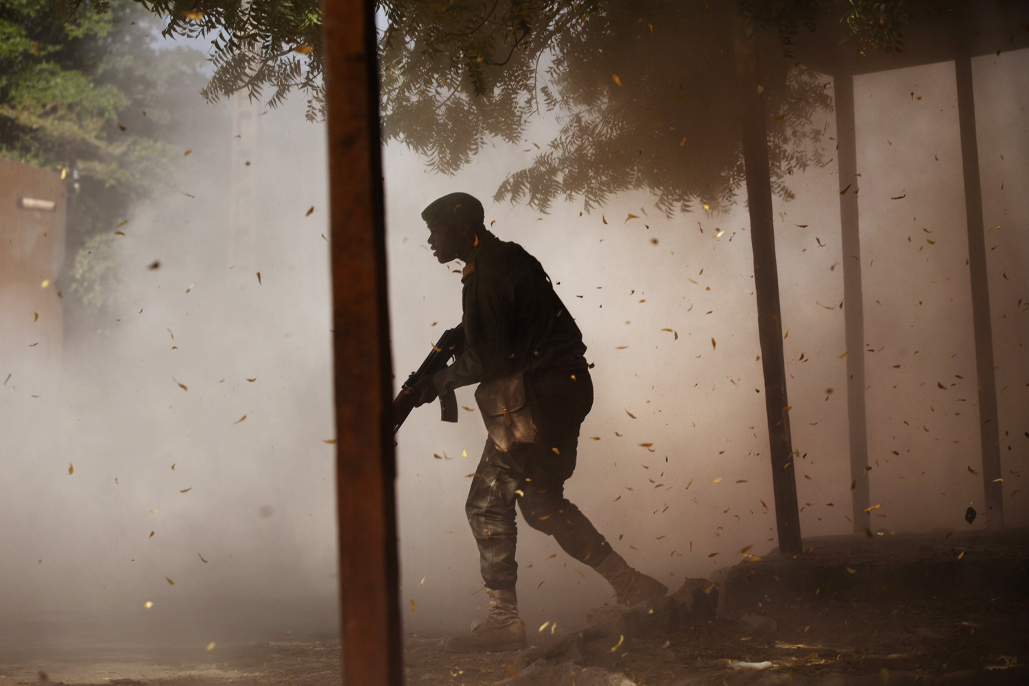 A Malian soldier takes cover amidst dust after a rocket propelled grenade was fired by his comrades in Gao