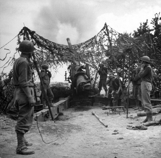 Camouflaged American artillery fires on German positions during Allied campaign in North Africa during WWII.