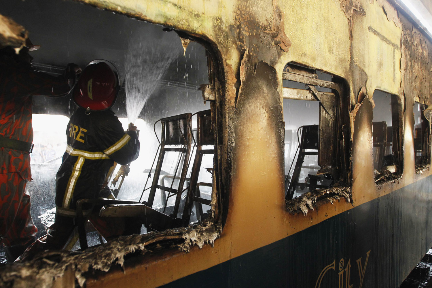 A fire fighter sprays water inside the burnt compartment of a train at Kamlapur Railway Station in Dhaka