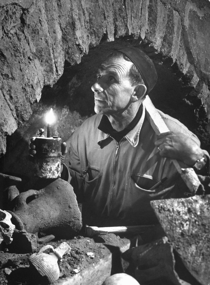 In a clutter of bones and artifacts the foreman of a team of Vatican workmen examines an ancient archway, St. Peter's, Rome, 1950.