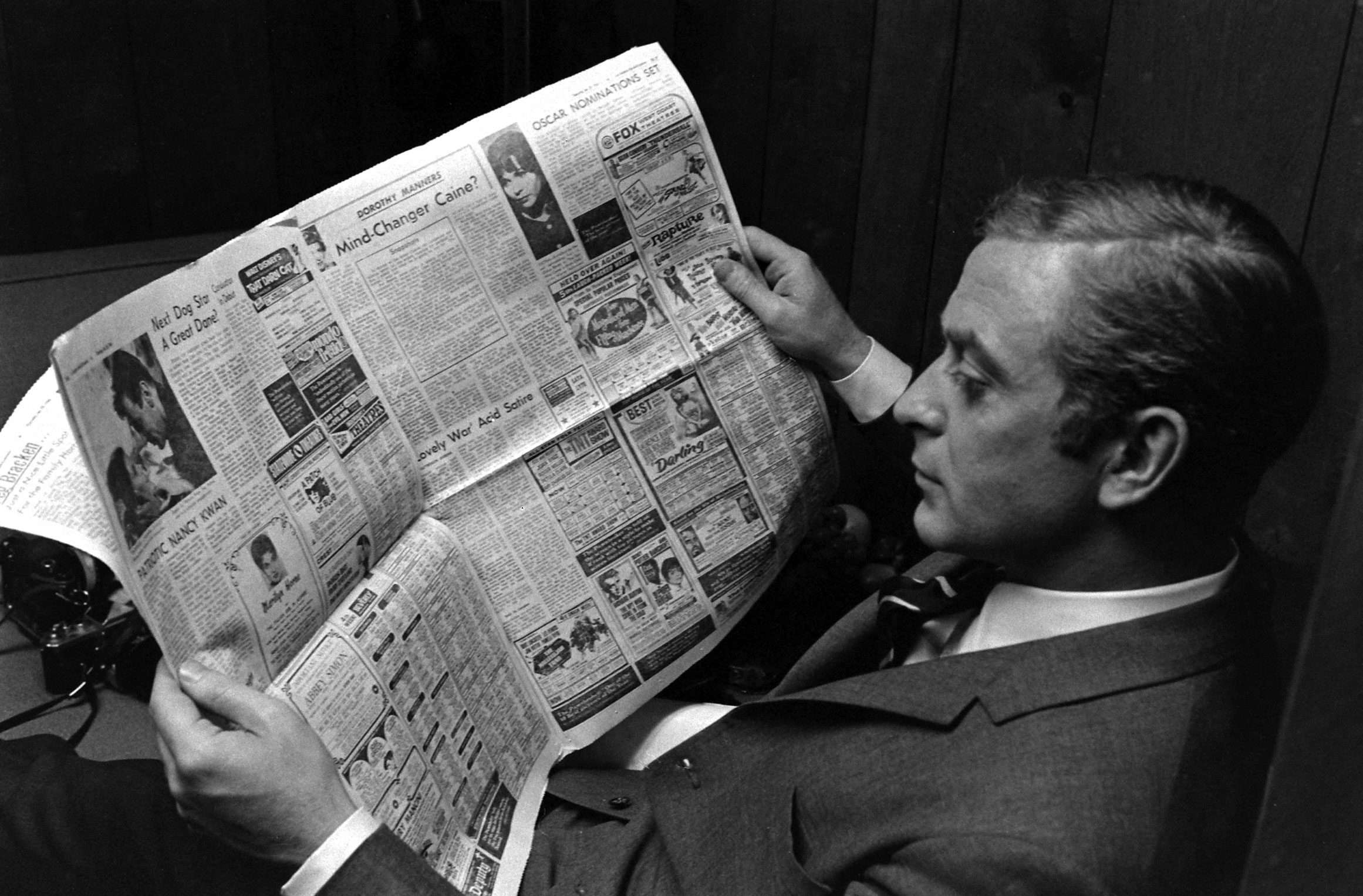 Michael Caine reads a paper, and an article about himself, in Los Angeles in 1966.