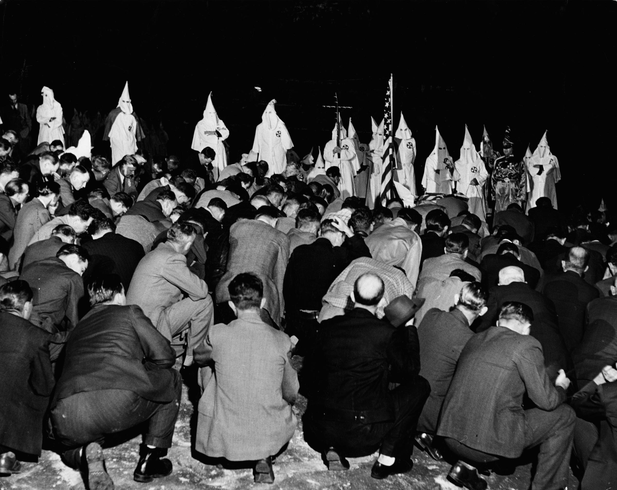 Klan initiates (including some Atlanta policemen) kneel before the local Grand Dragon during a ritual in Georgia, 1946.