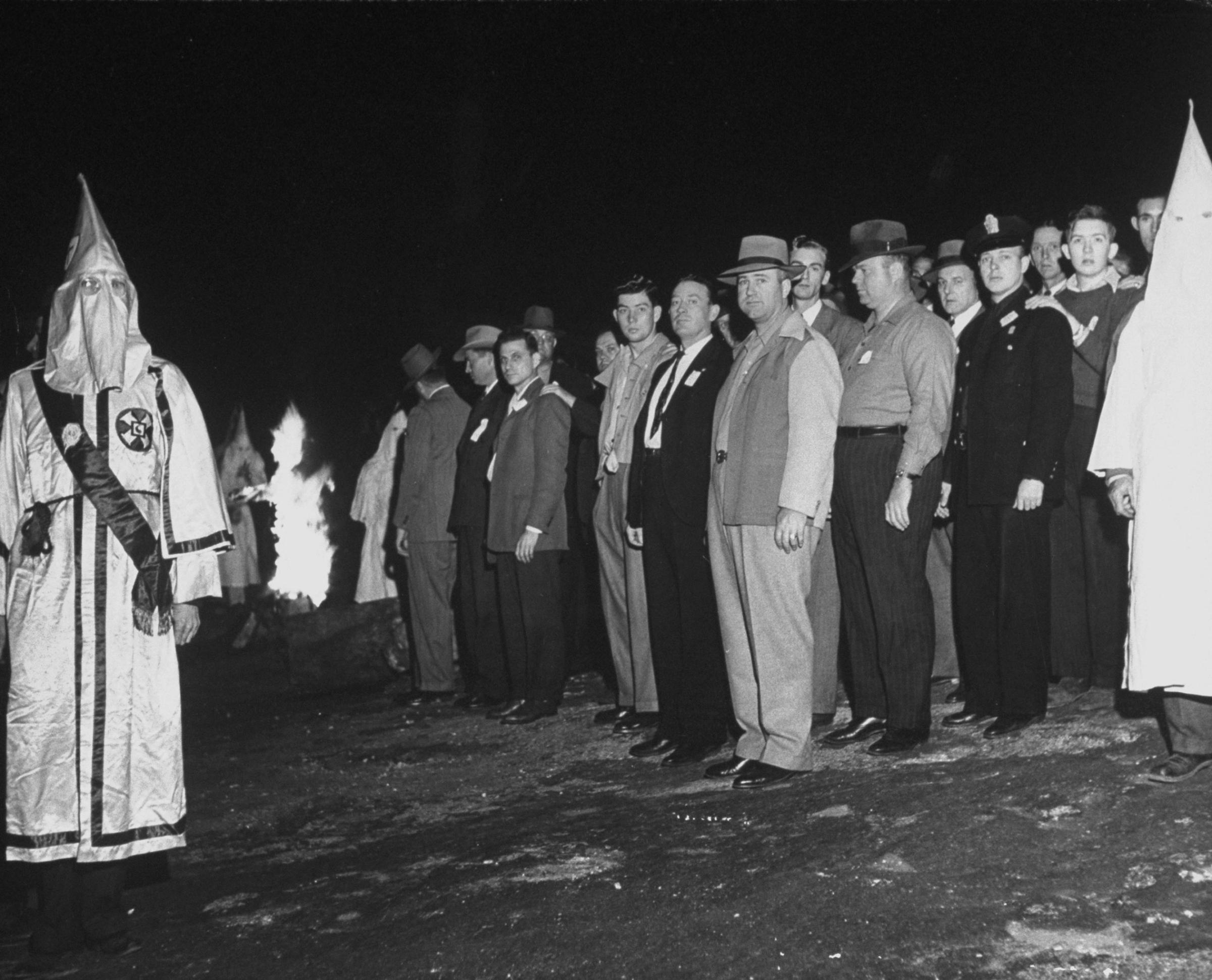 Klan initiates (including some Atlanta policemen) stand before a burning cross during a ritual in Georgia, 1946.