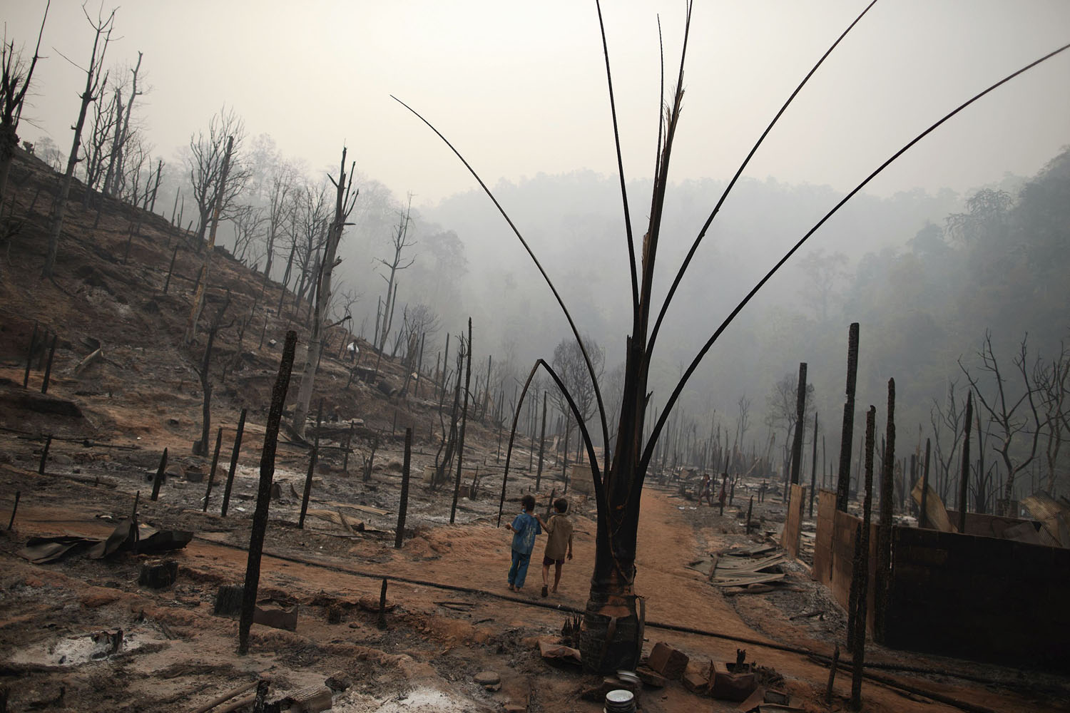 March 24, 2013. Two boys walk through the ruins of the Ban Mae Surin refugee camp near Mae Hong Son. At least 42 people have died in a fire at a camp which is home to thousands of refugees from Myanmar near the Thai-Myanmar border.