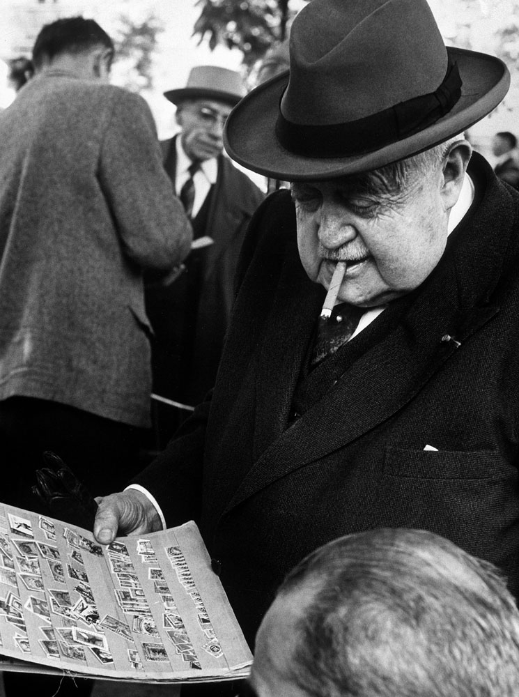 Man smoking cigar while examining stamps at stamp market on Avenue Matignon, Paris, 1963.