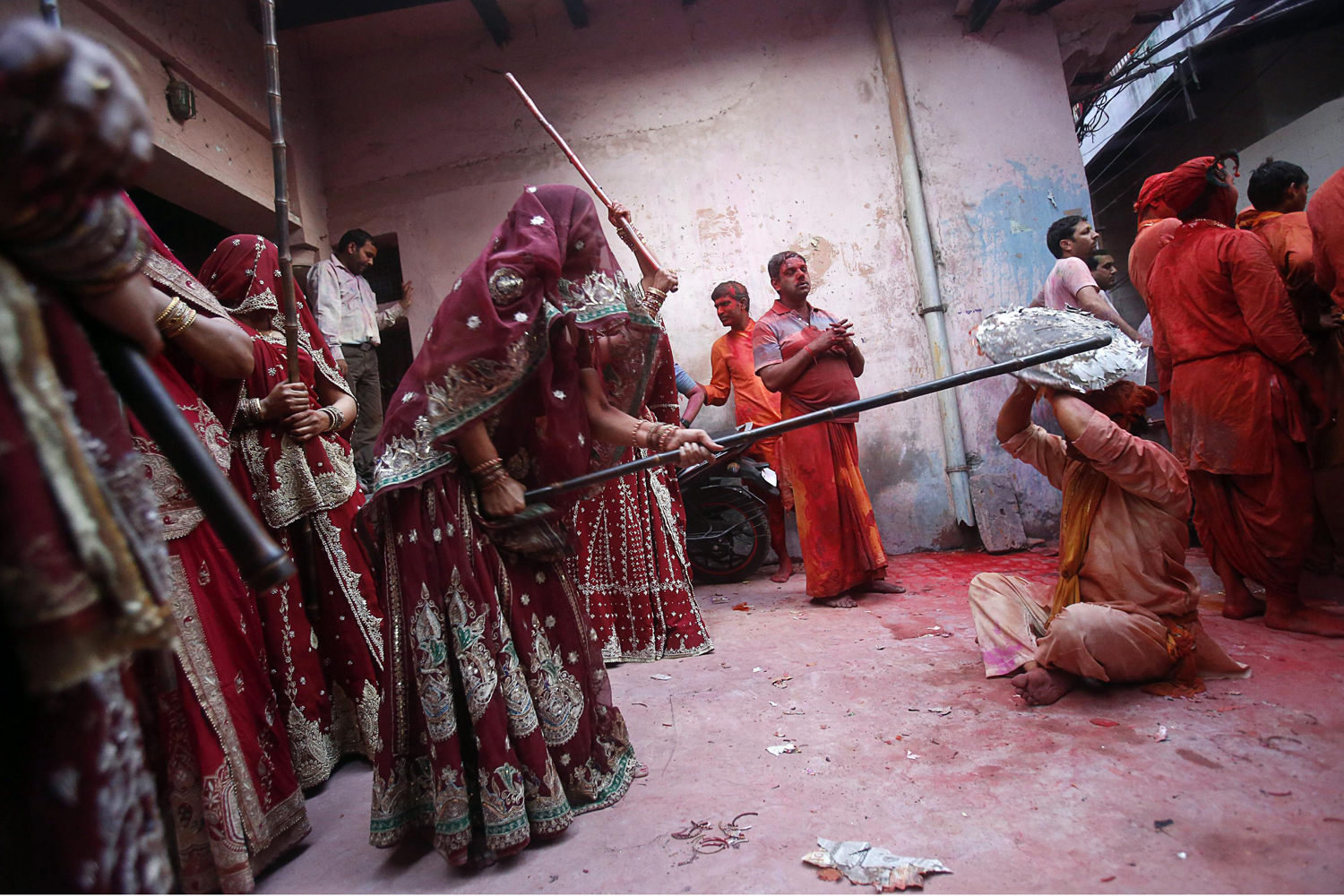 A group of women beat a man holding a shield over his head with sticks during Lathmar Holi at the village of Barsana