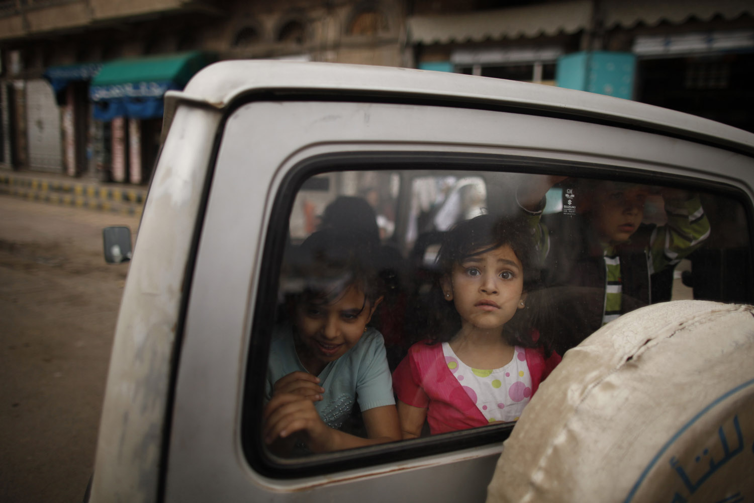 Children watch from the rear window of a car as protesters march past demanding Yemen's former President Saleh's immunity be stripped and that he stand trial in Sanaa