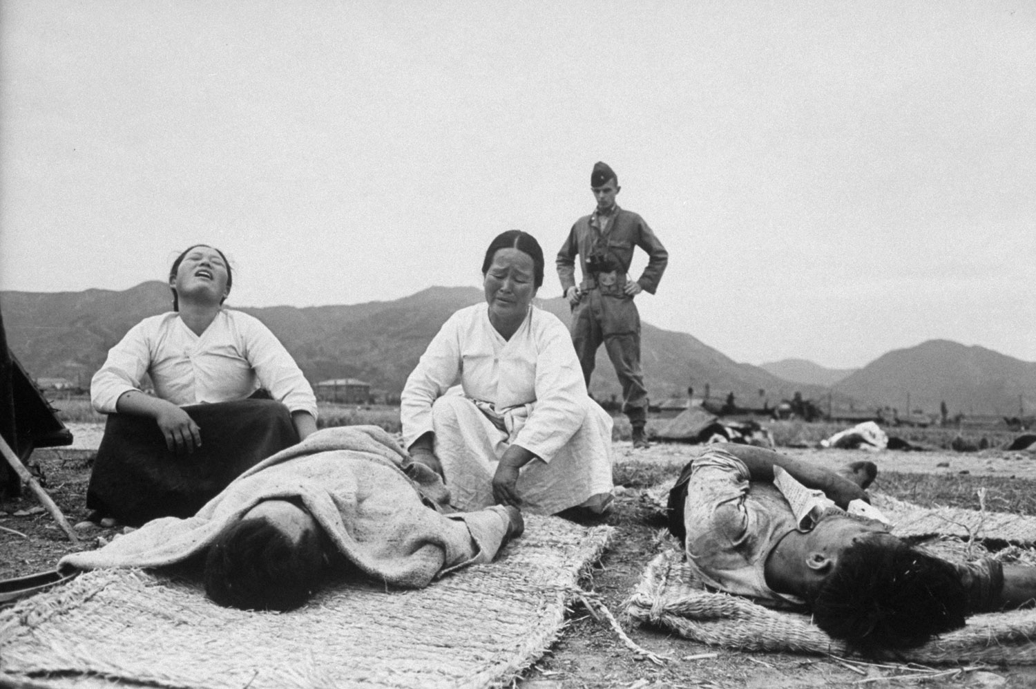 Two of Sunchon's bereaved women mourn a loyal Korean who fell before a rebel slaughter squad as the rebellion began. An American adviser, Lieut. Ralph Bliss, looks on silently where no advice will help.