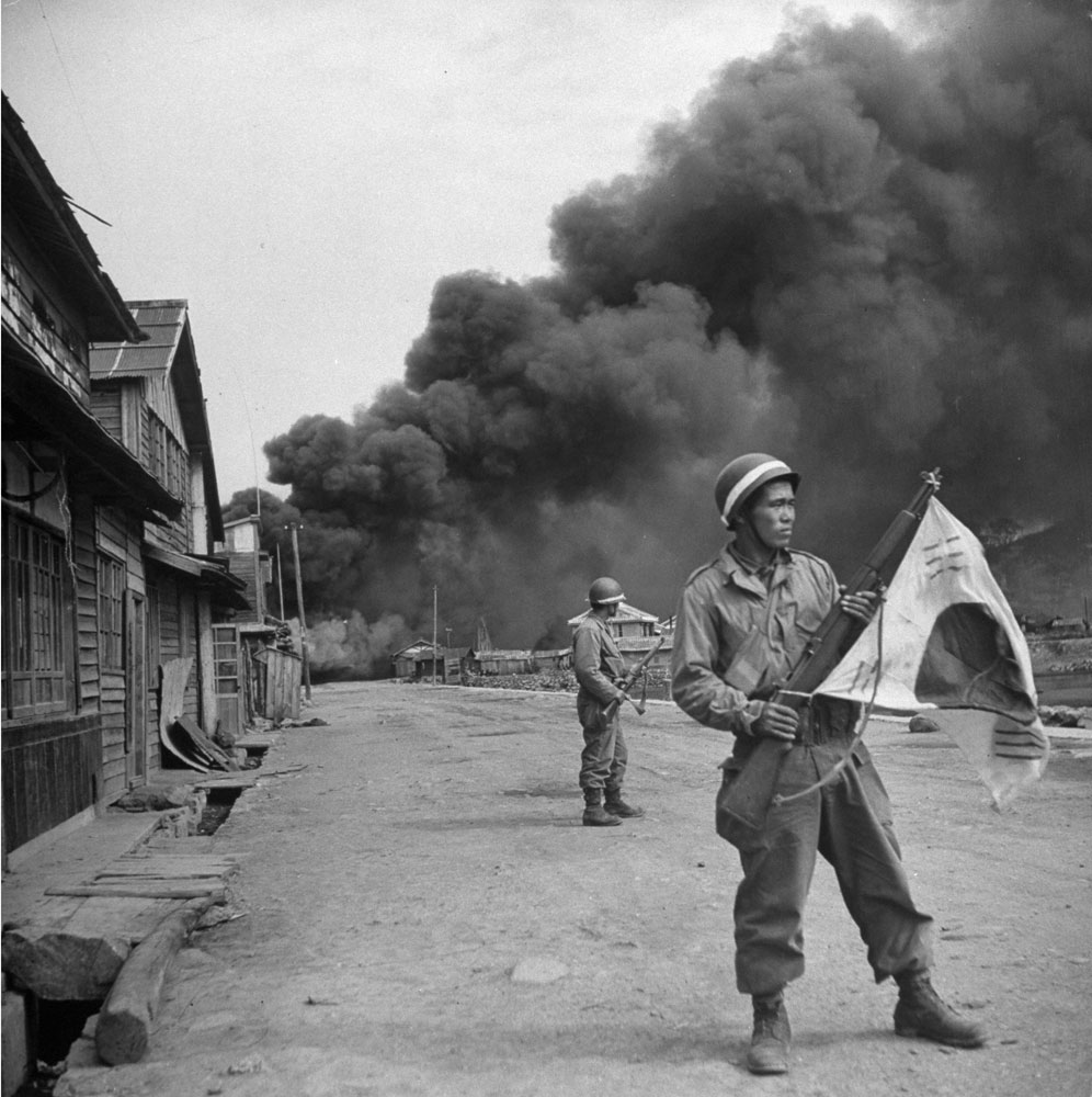 South Korean soldiers stand guard while a village burns during a communist uprising, 1948.