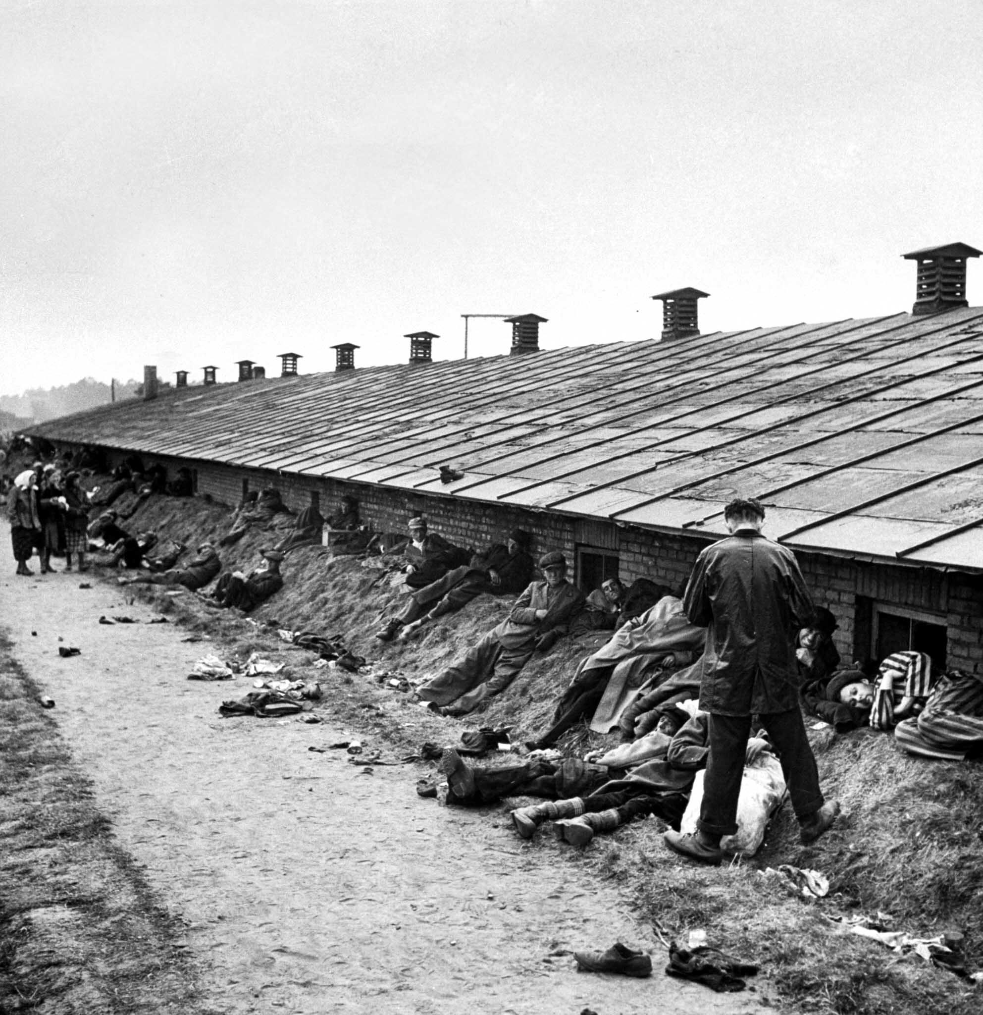 Dying men stretch out on a dirt bank behind one of the Bergen-Belsen barracks, 1945.