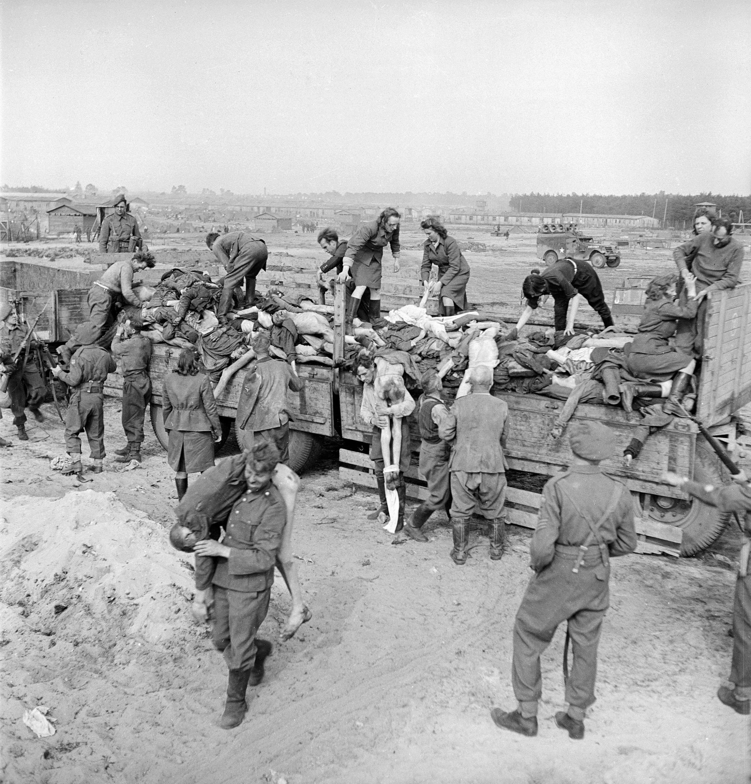 Male and female German SS soldiers forced to load corpses onto trucks under British guard at the Bergen-Belsen concentration camp, 1945.