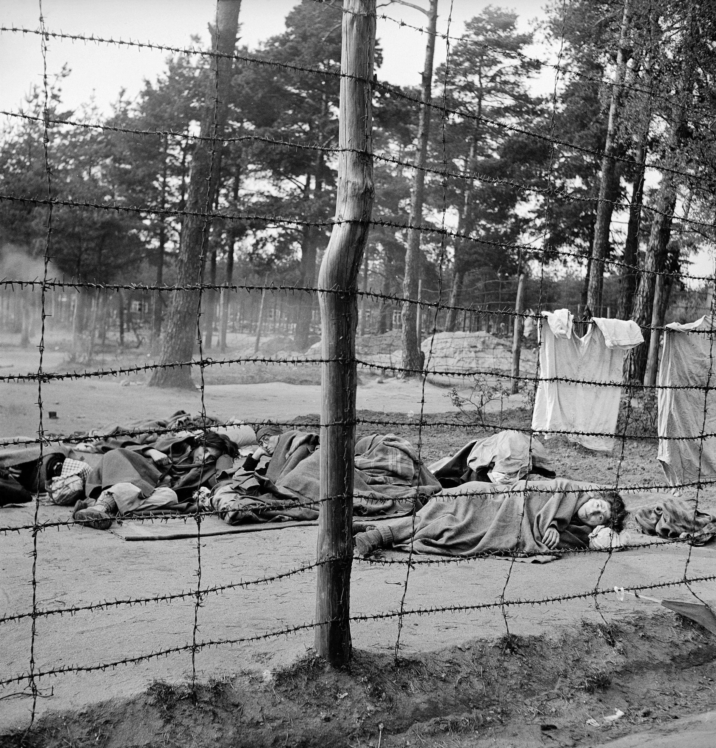 Dying women huddle on the ground behind the barbed-wire enclosure at Bergen-Belsen, 1945.