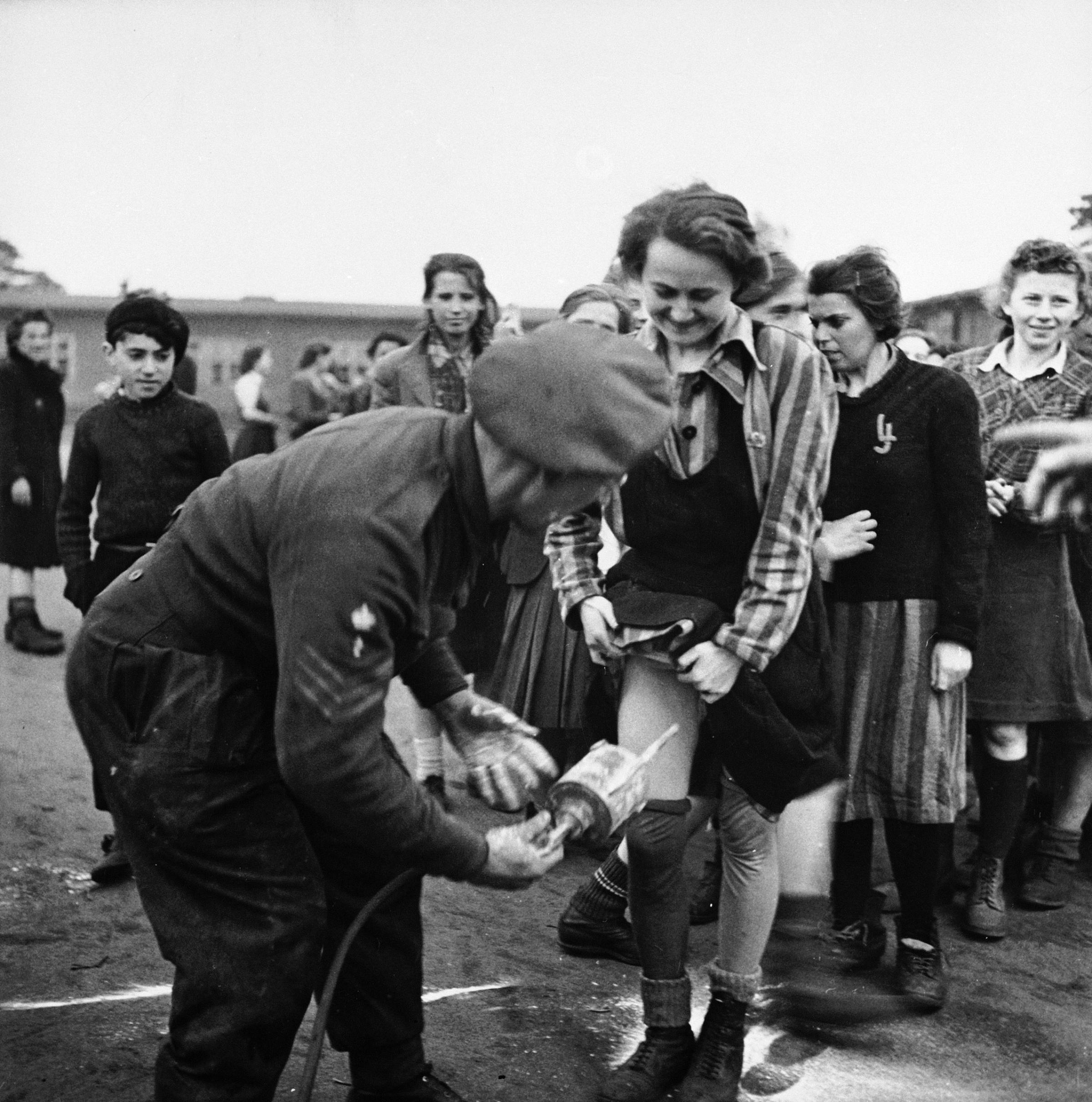 A British doctor administers delousing treatment of DDT up the skirt of an embarrassed-looking female prisoner at Bergen-Belsen, 1945.