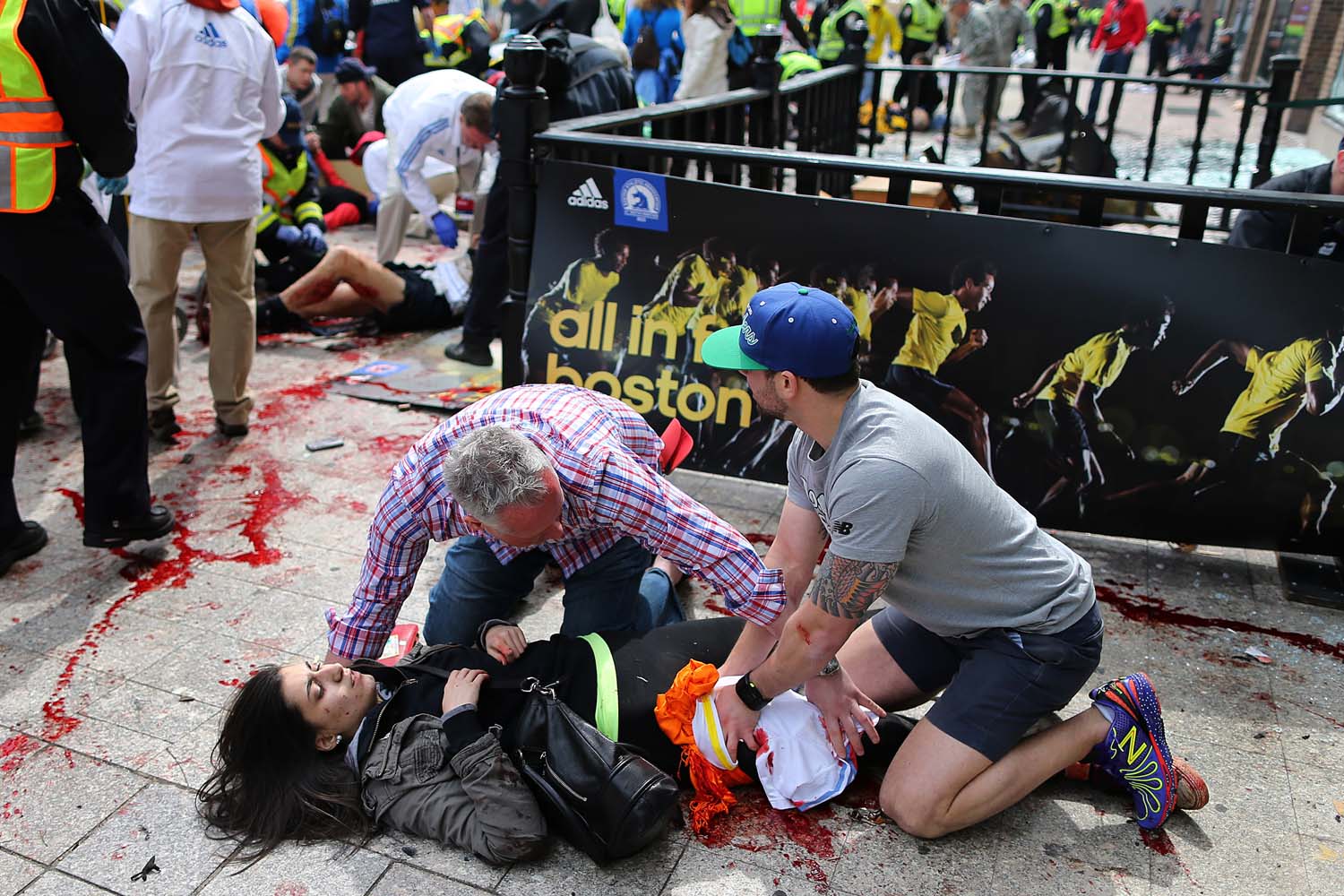 April 15, 2013. Bystanders help an injured woman at the scene of the first explosion on Boylston Street near the finish line of the 117th Boston Marathon.