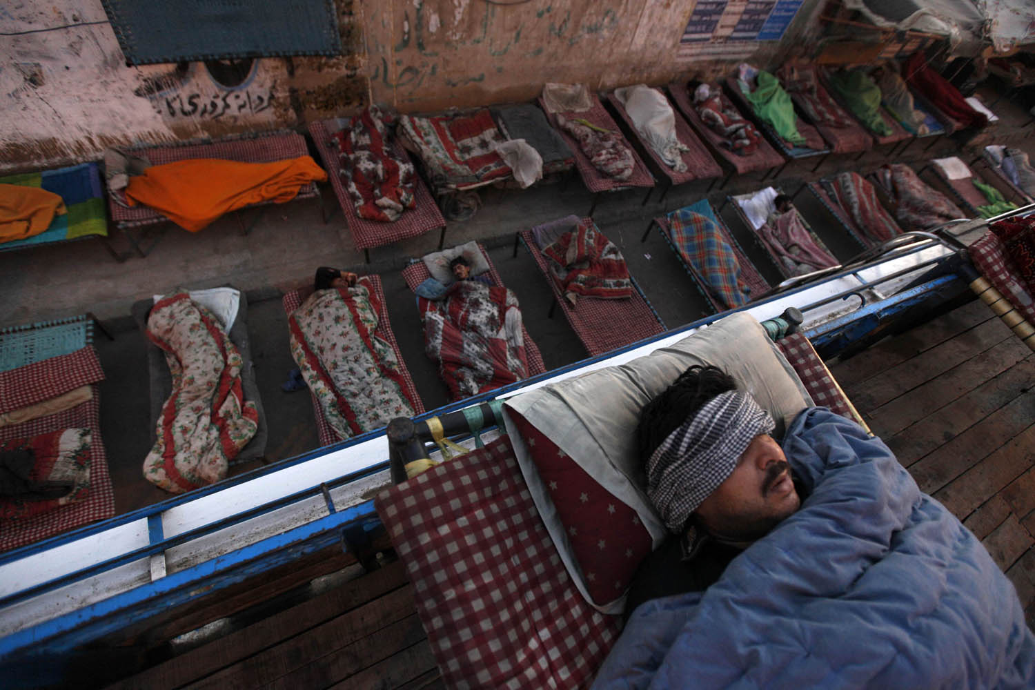 People sleep on charpoy beds along a road, near a railway station in Karachi