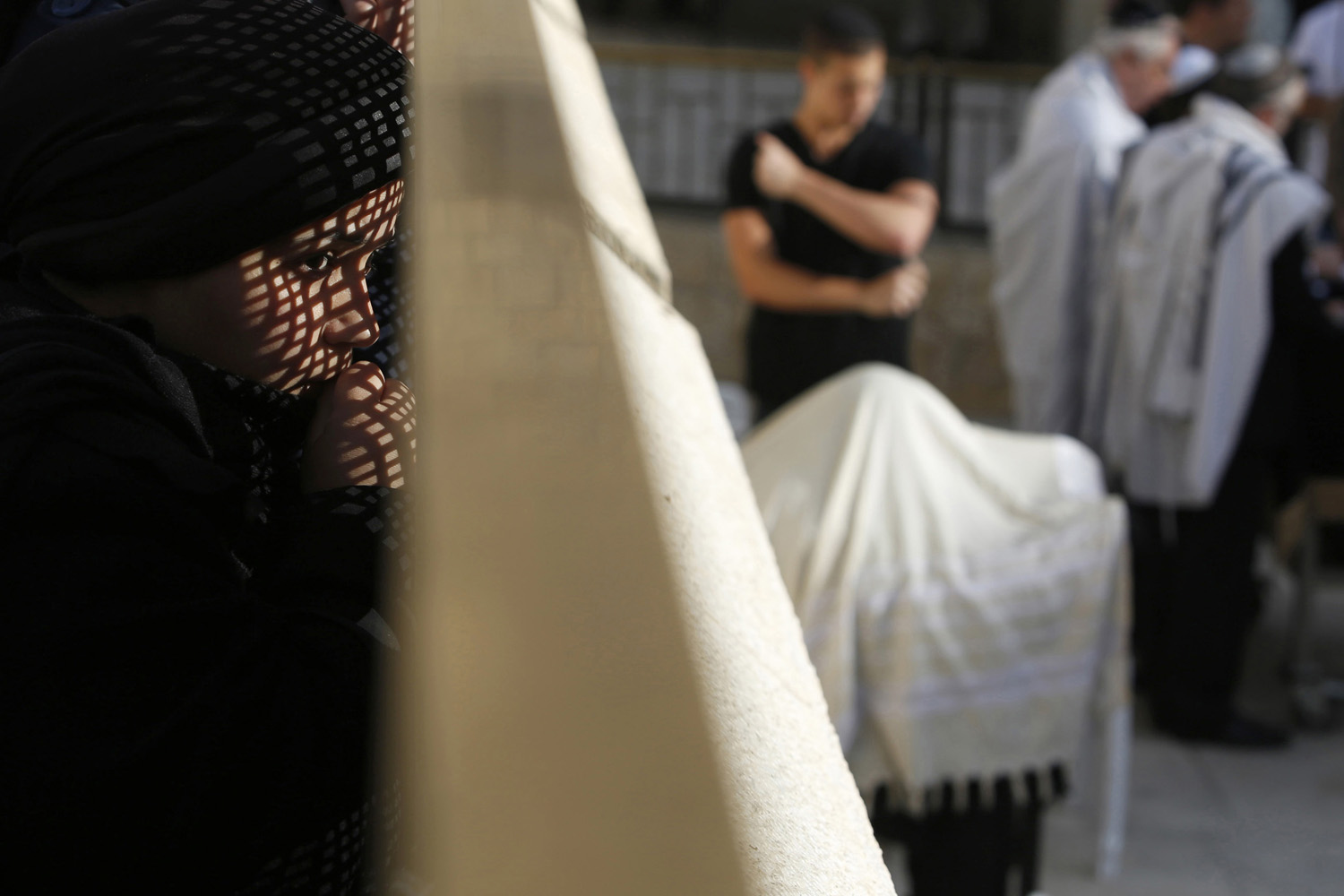 A woman looks at men praying from behind a metal screen at the Western Wall Judaism's holiest prayer site, in Jerusalem's Old City
