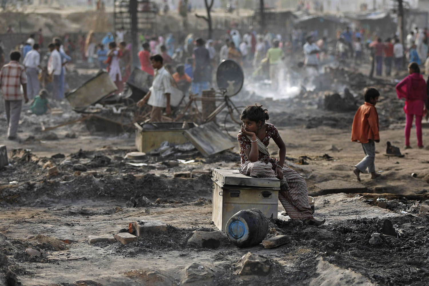 April 12, 2013. A local resident sits on a trunk amid the burnt debris of her hut after a fire broke out in a slum area in New Delhi.